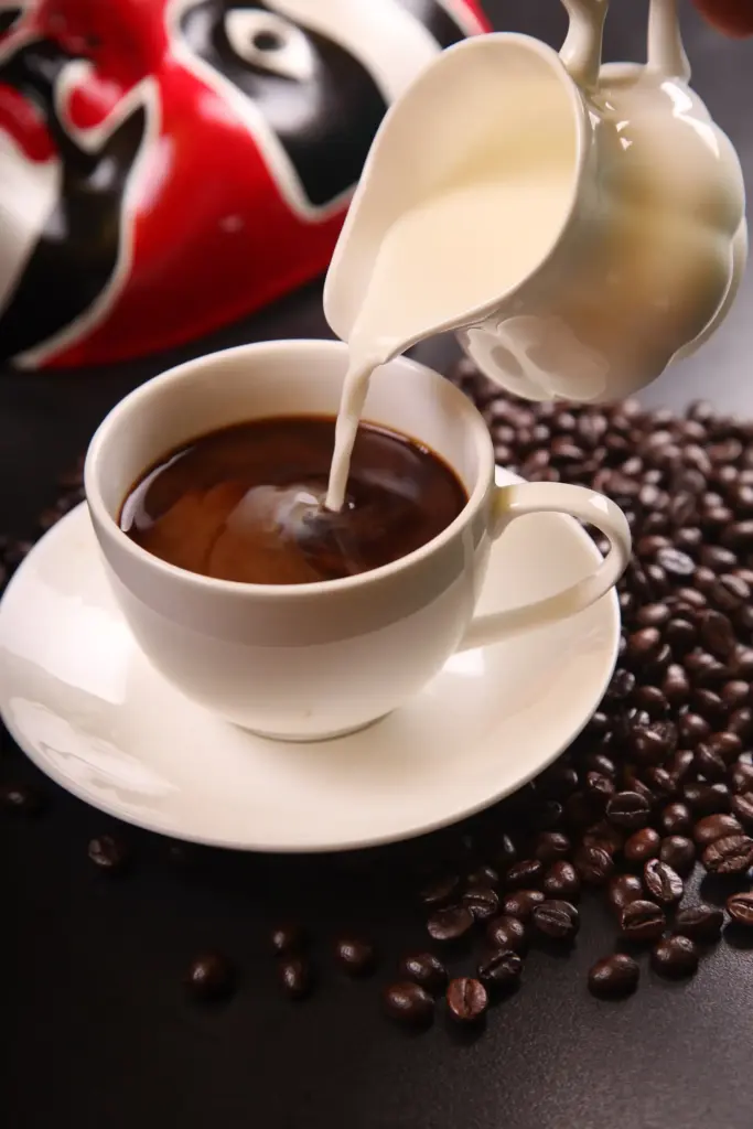 Coffee with milk being poured into a cup with roasted coffee beans, representing daily coffee consumption and its link to gut microbiome and cognitive effects