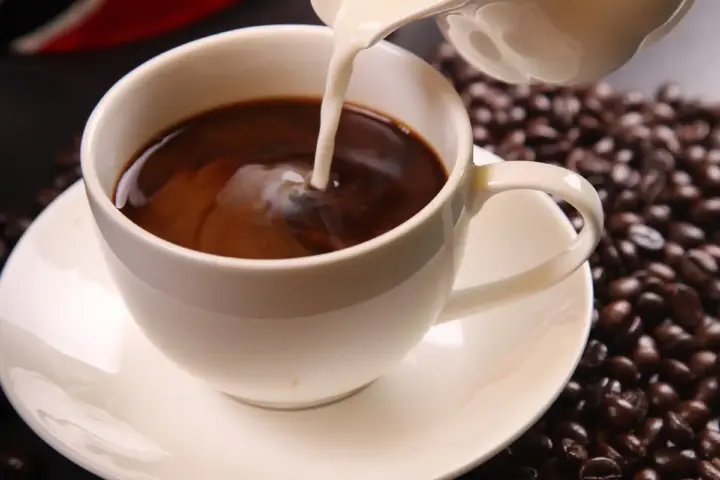 Coffee with milk being poured into a cup with roasted coffee beans, representing daily coffee consumption and its link to gut microbiome and cognitive effects