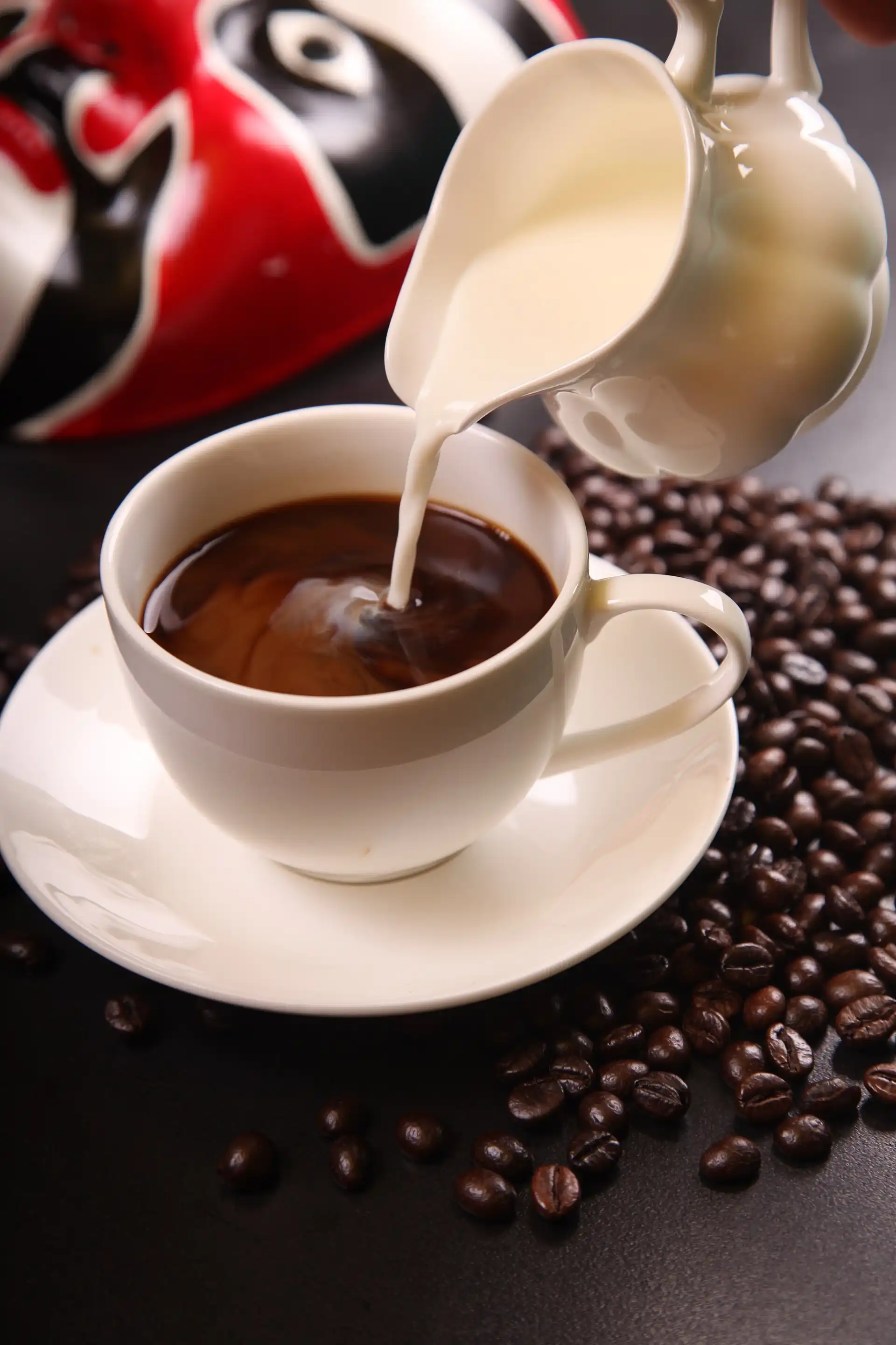 Coffee with milk being poured into a cup with roasted coffee beans, representing daily coffee consumption and its link to gut microbiome and cognitive effects