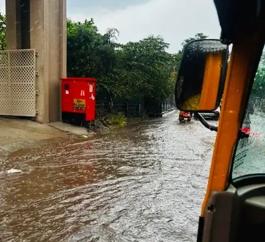 Flooded road in Pune with an auto rickshaw moving through rainwater during heavy unseasonal rainfall under overcast skies.