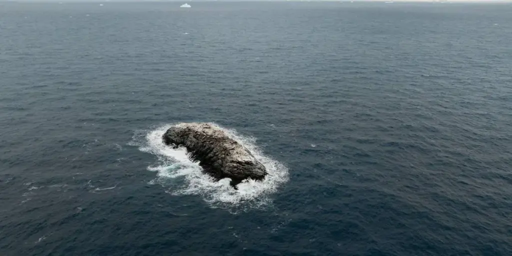 Ice-covered rocky island surrounded by ocean waves in the Weddell Sea, identified during the 2026 AWI Polarstern Antarctic expedition.