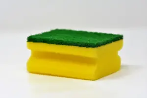 Yellow and green household cleaning sponge photographed against a white background, representing everyday cleaning products linked to microplastic fiber shedding.