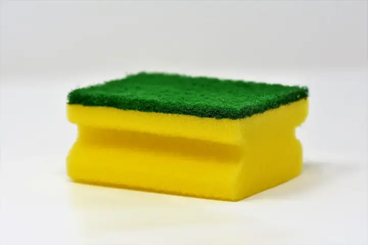 Yellow and green household cleaning sponge photographed against a white background, representing everyday cleaning products linked to microplastic fiber shedding.