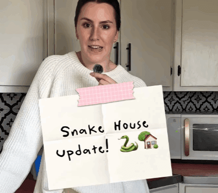 Callie holds a “Snake House Update!” sign inside her Montana farmhouse while discussing the ongoing garter snake issue linked to the home’s foundation.