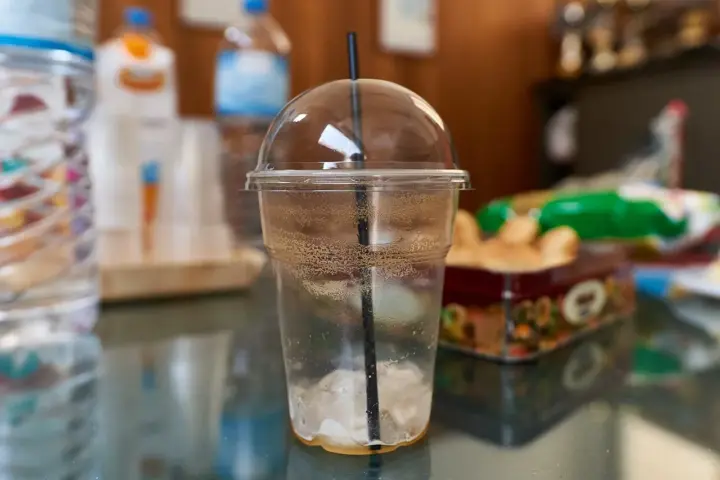 Disposable clear plastic cup with lid and straw on a table, illustrating single-use plastic packaging commonly associated with polypropylene waste streams and recycling challenges.