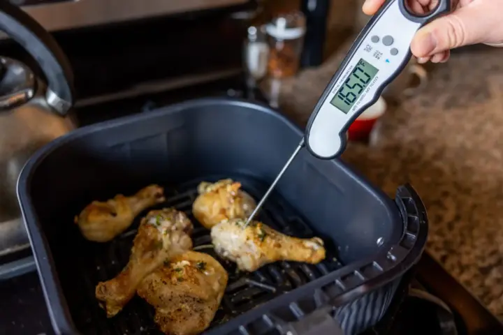 Digital food thermometer inserted into cooked chicken pieces showing internal temperature measurement for Salmonella safety verification