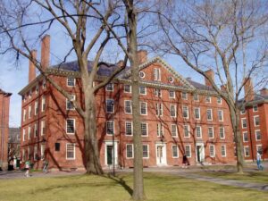 Hollis Hall, a historic brick building at Harvard University in Cambridge, Massachusetts, viewed from across a grassy lawn on a sunny day.