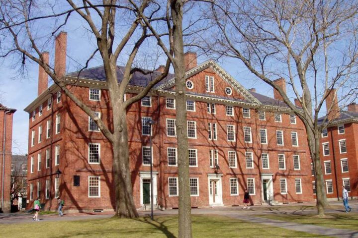 Hollis Hall, a historic brick building at Harvard University in Cambridge, Massachusetts, viewed from across a grassy lawn on a sunny day.
