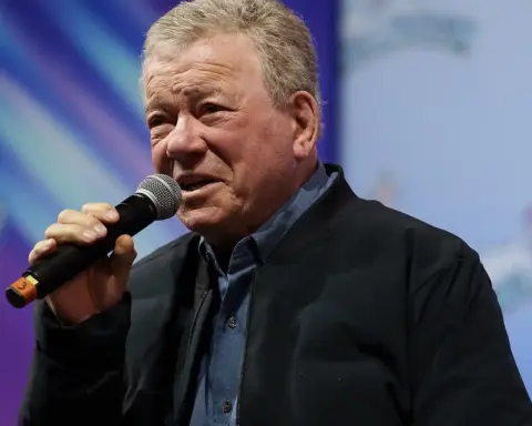 William Shatner, age 95, holding a microphone while speaking at a public event in December 2025, following his recovery from Stage 4 melanoma diagnosis.