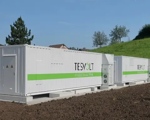 White containerised battery energy storage units (BESS) in a rural field with cooling units on the roof.