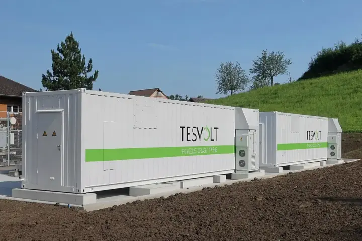 White containerised battery energy storage units (BESS) in a rural field with cooling units on the roof.