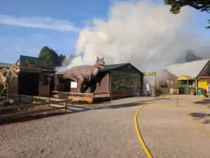 Entrance of Hoo Zoo and Dinosaur World with a T-Rex statue and smoke from the August 2026 fire.