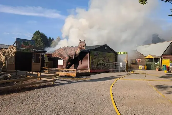 Entrance of Hoo Zoo and Dinosaur World with a T-Rex statue and smoke from the August 2026 fire.