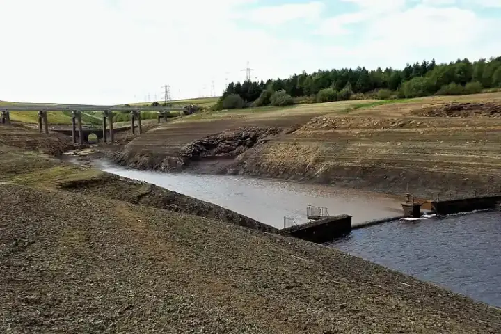 A largely dry reservoir bed with exposed cracked banks and a thin strip of water, England.