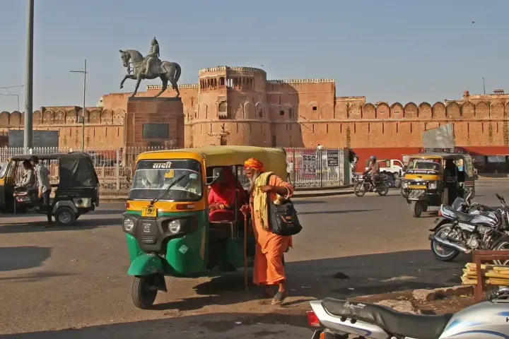 Green and yellow auto-rickshaw picking up a passenger outside Junagarh Fort in Bikaner, Rajasthan.