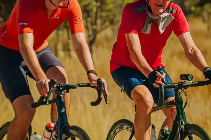 Two cyclists riding side-by-side on a rural road during a charity ride.