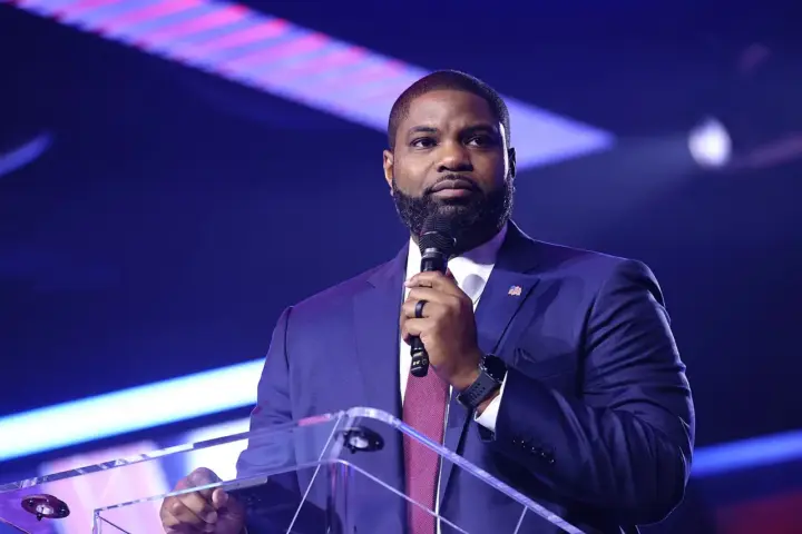 U.S. Representative Byron Donalds speaking at a podium with an American flag pin.