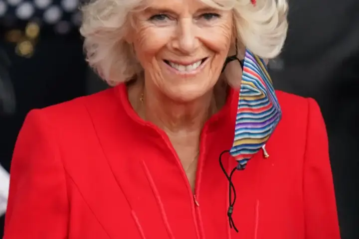 Queen Camilla of the United Kingdom smiling in a red coat and matching hat at a public engagement.