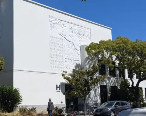 Exterior of a high school building in the United States with relief sculpture on white facade and parked vehicles on street