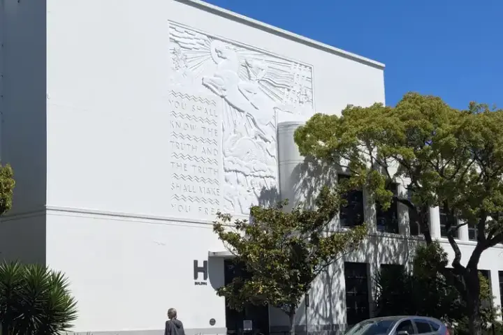 Exterior of a high school building in the United States with relief sculpture on white facade and parked vehicles on street