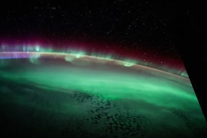 Northern Lights (Aurora Borealis) dancing across a star-filled night sky with green and pink curtains of light