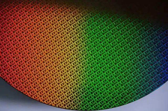 A semiconductor silicon wafer showing die patterns with rainbow coating - representing Intel Foundry 18A process technology.