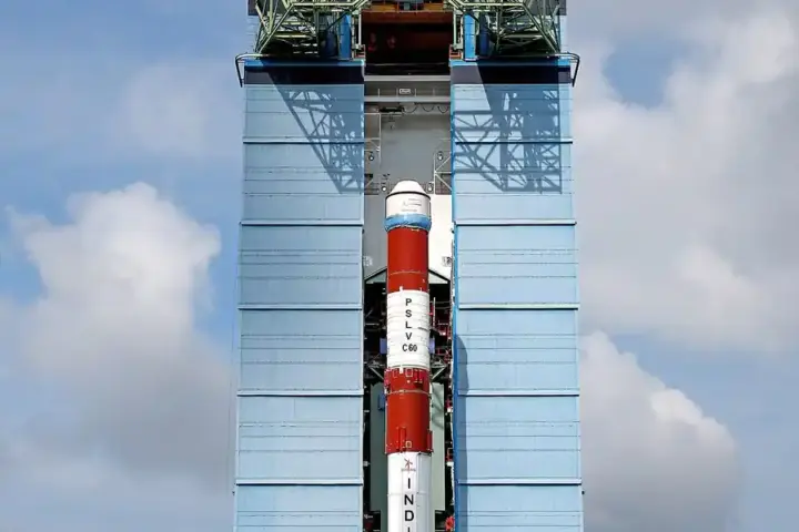ISRO's PSLV-C60 launch vehicle on the launch pad at Satish Dhawan Space Centre, Sriharikota, with ground staff in high-visibility vests behind a safety fence.