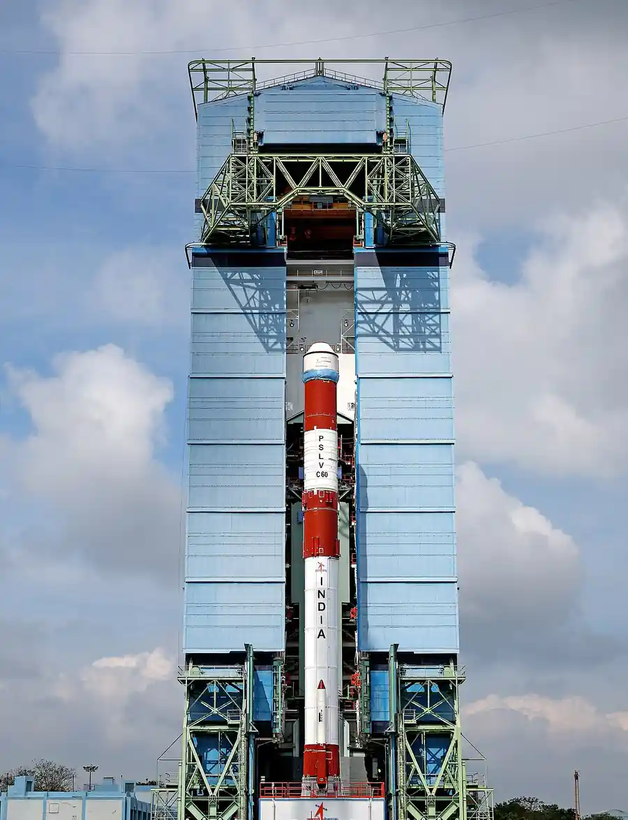 ISRO's PSLV-C60 launch vehicle on the launch pad at Satish Dhawan Space Centre, Sriharikota, with ground staff in high-visibility vests behind a safety fence.