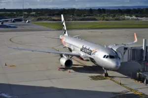 A Jetstar Airbus A320 parked at an airport gate with a jet bridge attached.