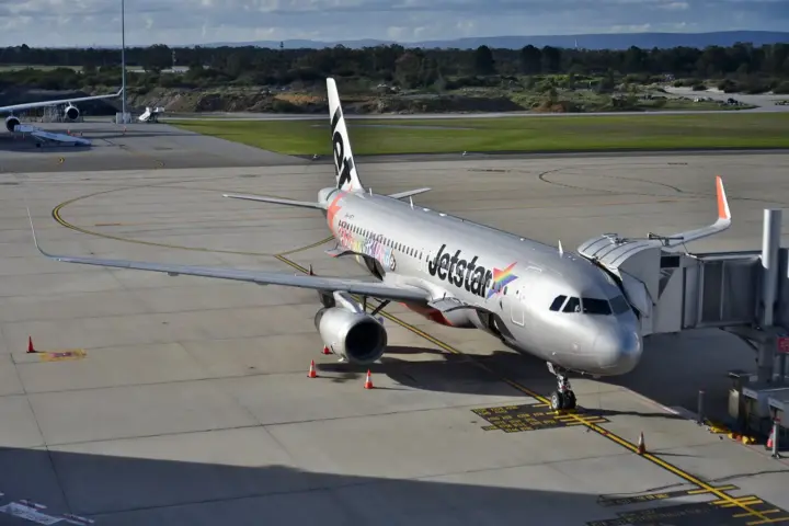 A Jetstar Airbus A320 parked at an airport gate with a jet bridge attached.
