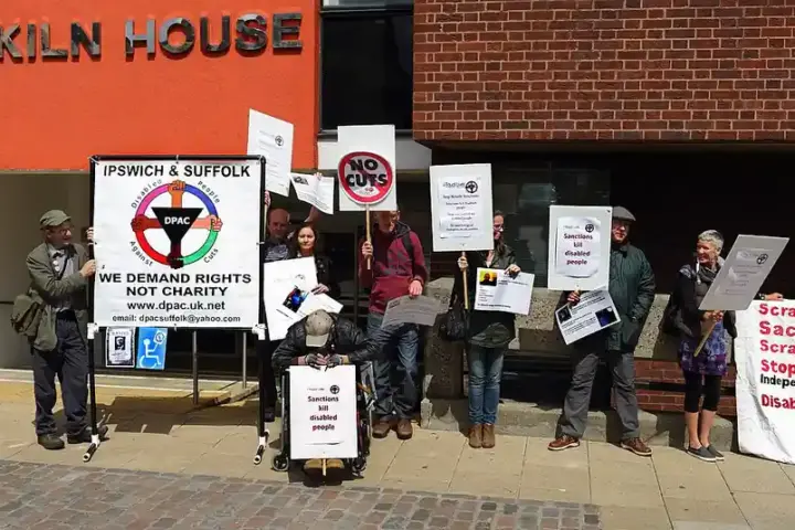 Disabled activists demonstrating outside a Department for Work and Pensions building with anti-cuts banners.