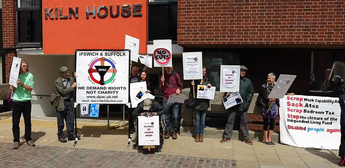 Disabled activists demonstrating outside a Department for Work and Pensions building with anti-cuts banners.