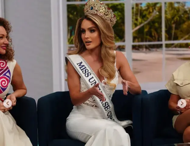 Mia Dio, crowned Miss Universe Cuba 2026, seated wearing her ornate crown and white sash with "MISS UN..." lettering. She wears a white gown with silver sequin bodice. Source: Mia Dio Instagram.