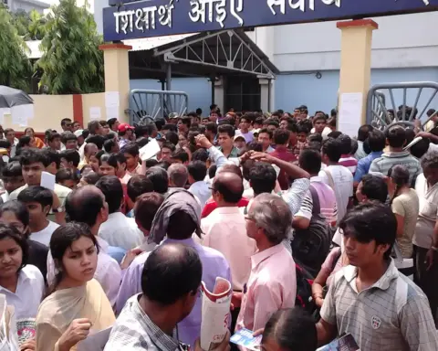 Large crowd of medical entrance exam candidates holding admit cards outside an examination centre gate in India.