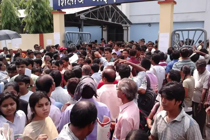 Large crowd of medical entrance exam candidates holding admit cards outside an examination centre gate in India.