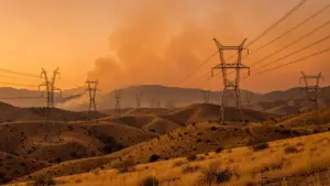 Power transmission lines across dry California hills under a smoky wildfire-threatened sky