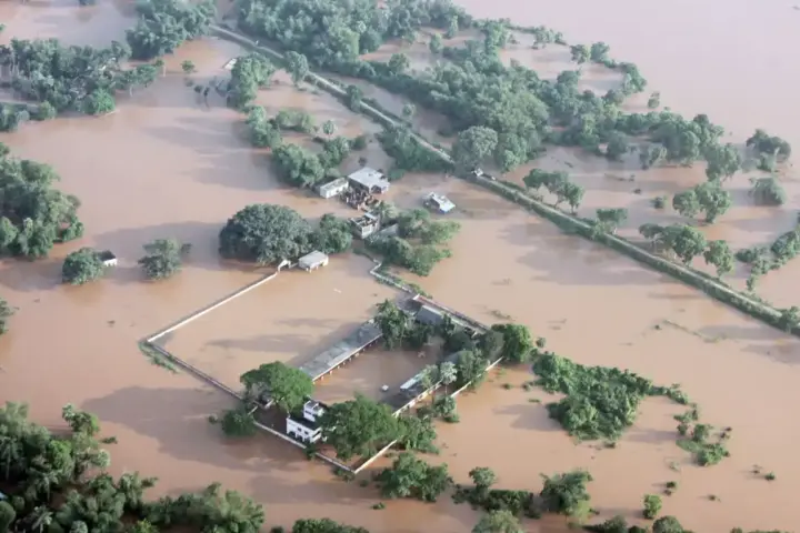 Aerial photograph of flooded villages in Balasore, Odisha, with homes and farmland submerged under muddy brown river water.