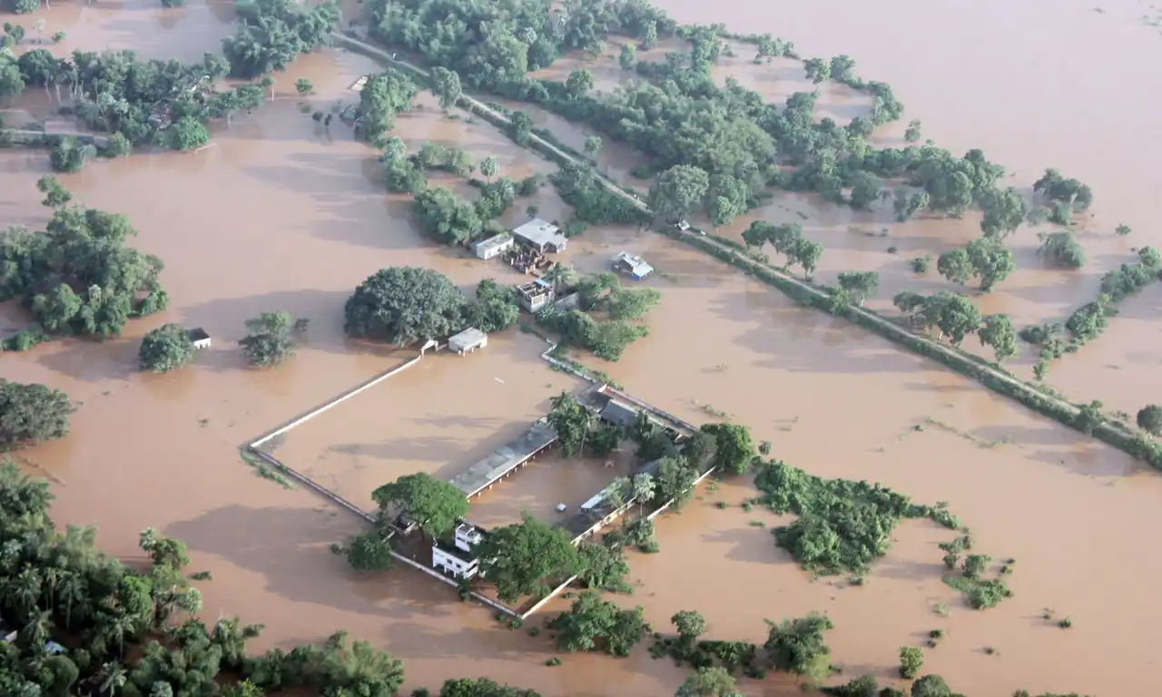 Aerial photograph of flooded villages in Balasore, Odisha, with homes and farmland submerged under muddy brown river water.