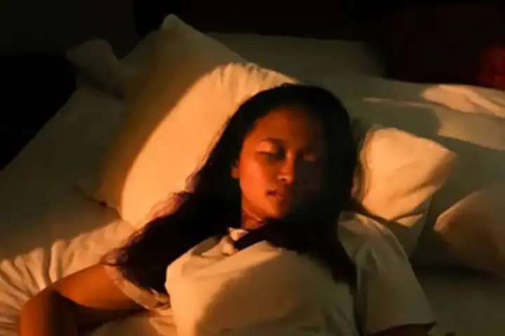 A woman sleeping peacefully in bed, bathed in warm golden sunlight, with pillows and bedding visible
