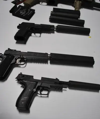 Several handguns with attached suppressors arranged on a dark surface, showing different makes and calibers.