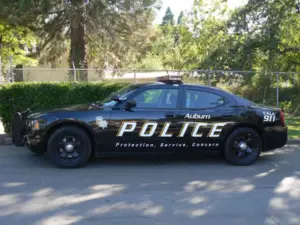 A white and black Dodge Charger police interceptor parked on a city street with emergency lights, representing the reach of automated license plate surveillance.