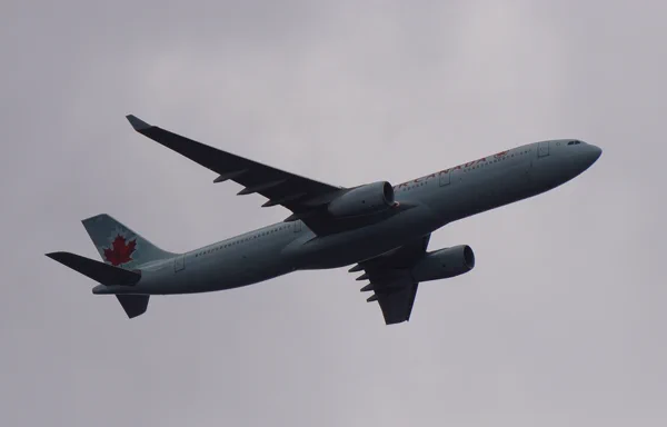 An Airbus A330-300 passenger jet flying at cruising altitude, with the sun visible on the horizon.