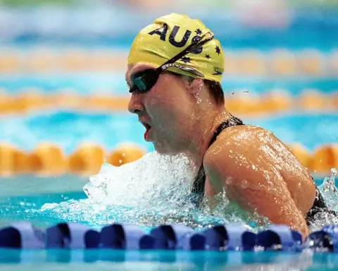 Competitive swimmer in a black racing suit and yellow cap swimming in a marked pool lane during a race.