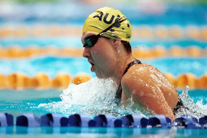 Competitive swimmer in a black racing suit and yellow cap swimming in a marked pool lane during a race.