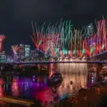 Fireworks illuminating the Brisbane River reach, bridges, and surrounding city buildings at dusk.