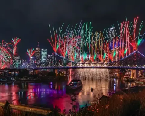 Fireworks illuminating the Brisbane River reach, bridges, and surrounding city buildings at dusk.