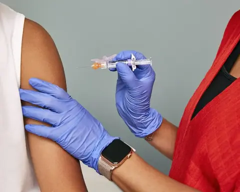 Close-up of gloved clinician preparing to administer a vaccine injection into a patient arm