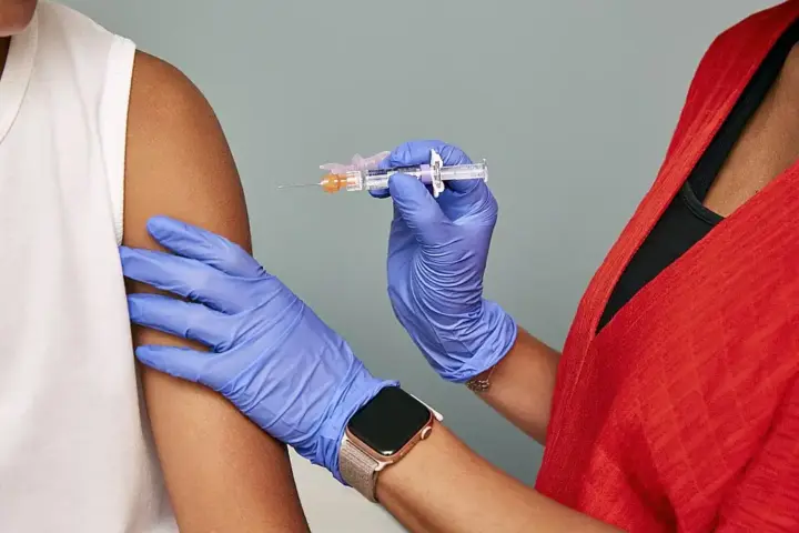 Close-up of gloved clinician preparing to administer a vaccine injection into a patient arm