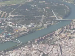 High-altitude aerial photograph of the urban landscape of Seville and surrounding agricultural land under bright daylight.