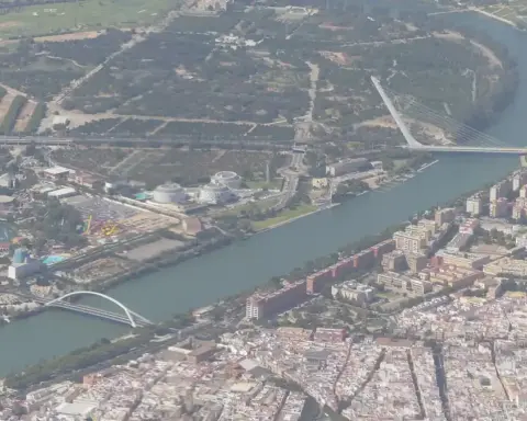 High-altitude aerial photograph of the urban landscape of Seville and surrounding agricultural land under bright daylight.